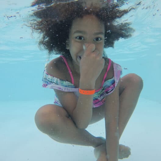 A young girl at an Iowa summer camp holding her nose underwater.