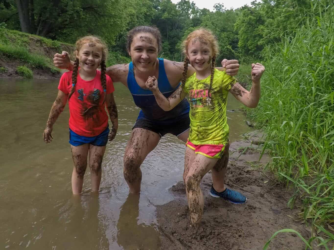 Two girls standing in a muddy river during summer camp in Iowa.