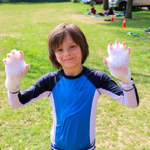 A young boy in blue shorts at summer camp in Iowa showing soap bubbles on his hands.