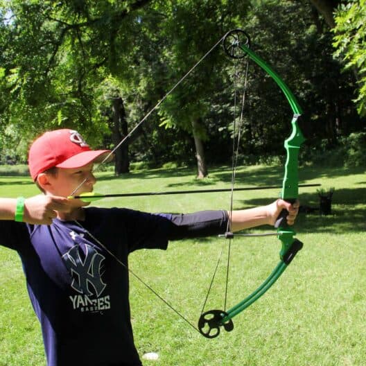 A young boy aiming a green bow during summer camp in Iowa.