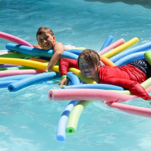 Two kids at a summer camp in Iowa swim with colorful floats in a pool.
