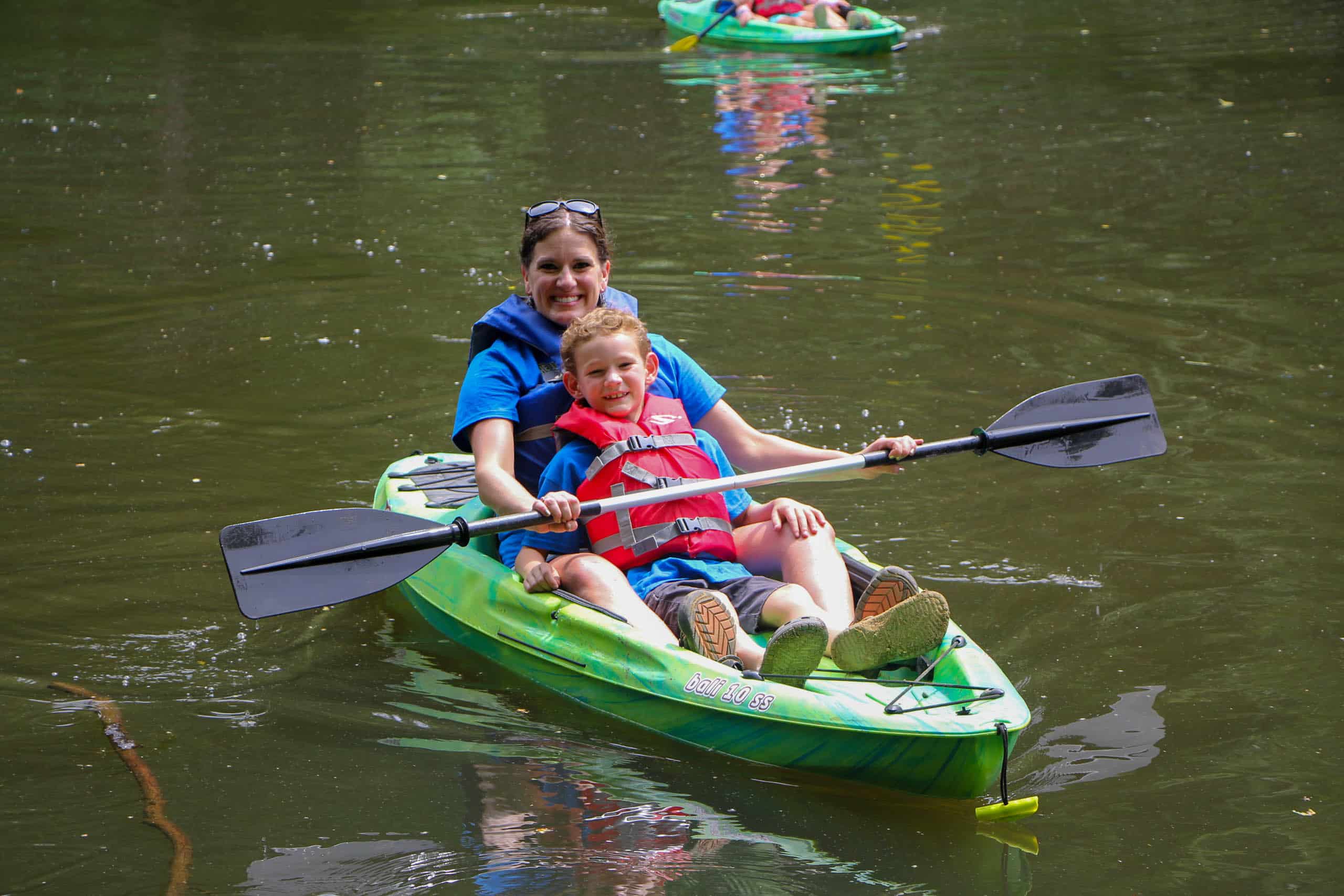 A kid and his mom paddle a green canoe at summer camp in Iowa.