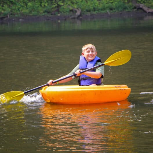 A young boy paddling a kayak in Iowa during summer camp.