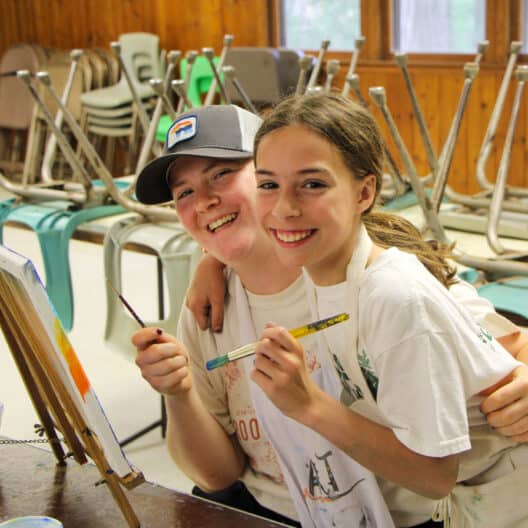 At a summer camp in Iowa, two girls are holding paint brushes.