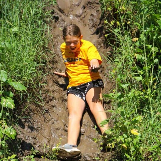 A girl sliding down on a muddy trail at summer camp in Iowa.