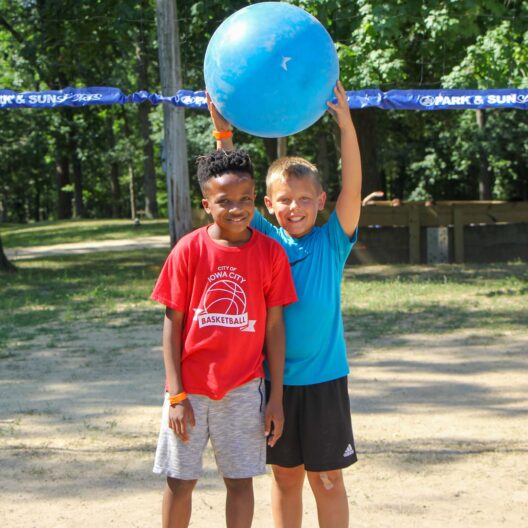 Two kids attending summer camp in Iowa playing with a blue ball.