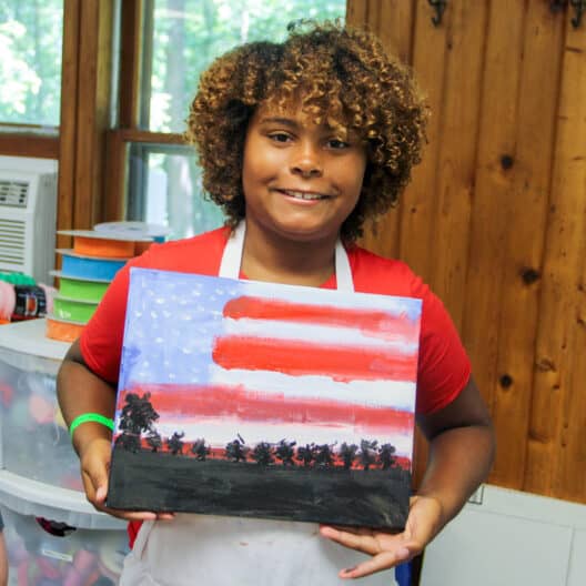 A kid holding up a painting of an American flag at summer camp in Iowa.