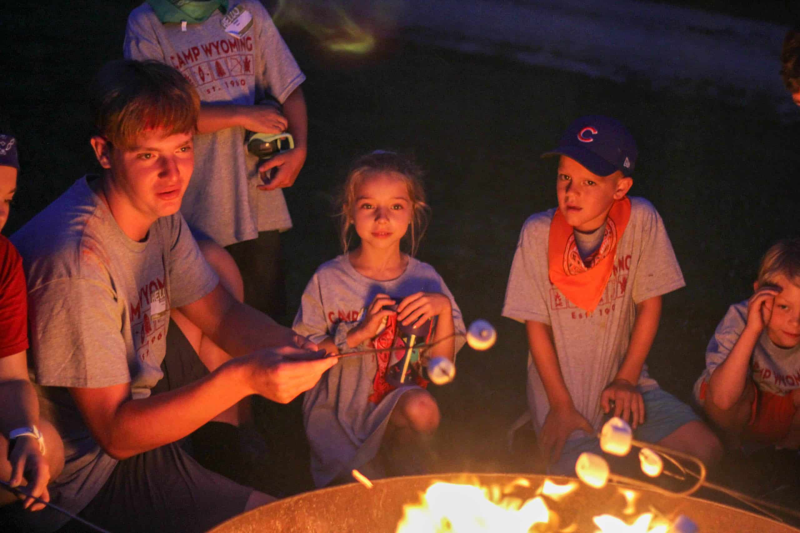 A group of kids at summer camp in Iowa sitting around a campfire with marshmallows.