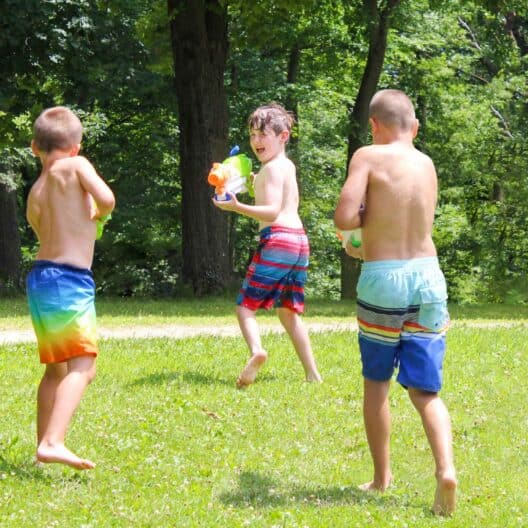 Three boys playing with water guns during summer camp in Iowa.