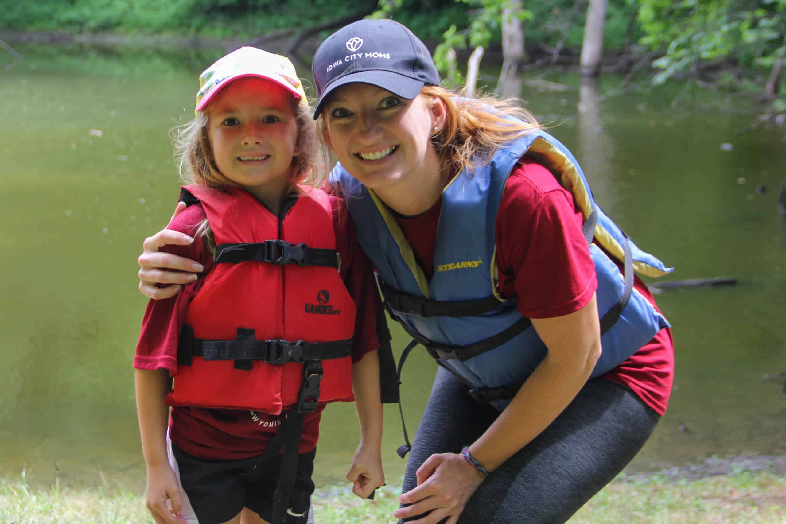 A young girl in a life jacket enjoys summer camp in Iowa with her counselor.