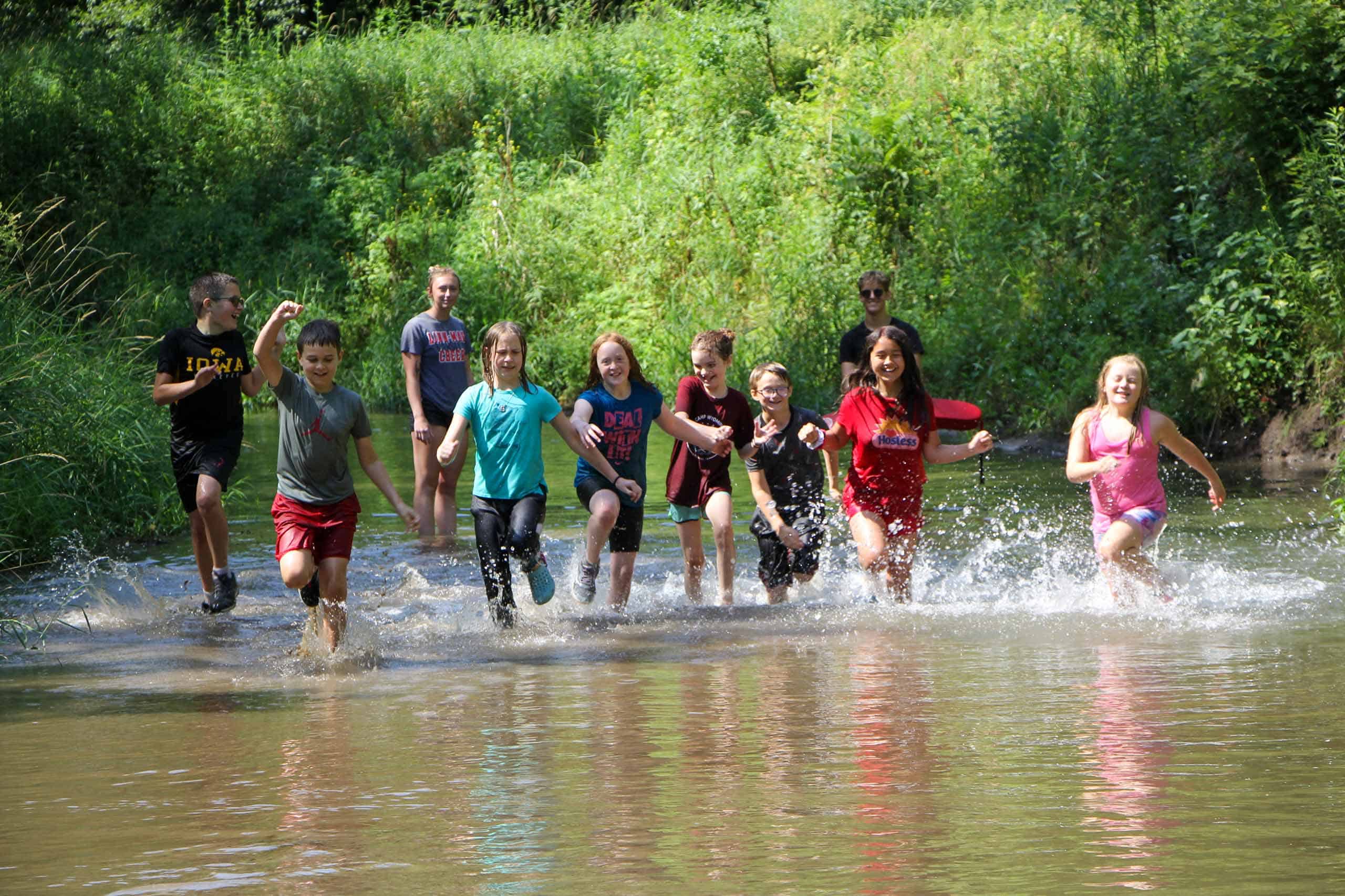 A group of kids at summer camp running through a river in Iowa.