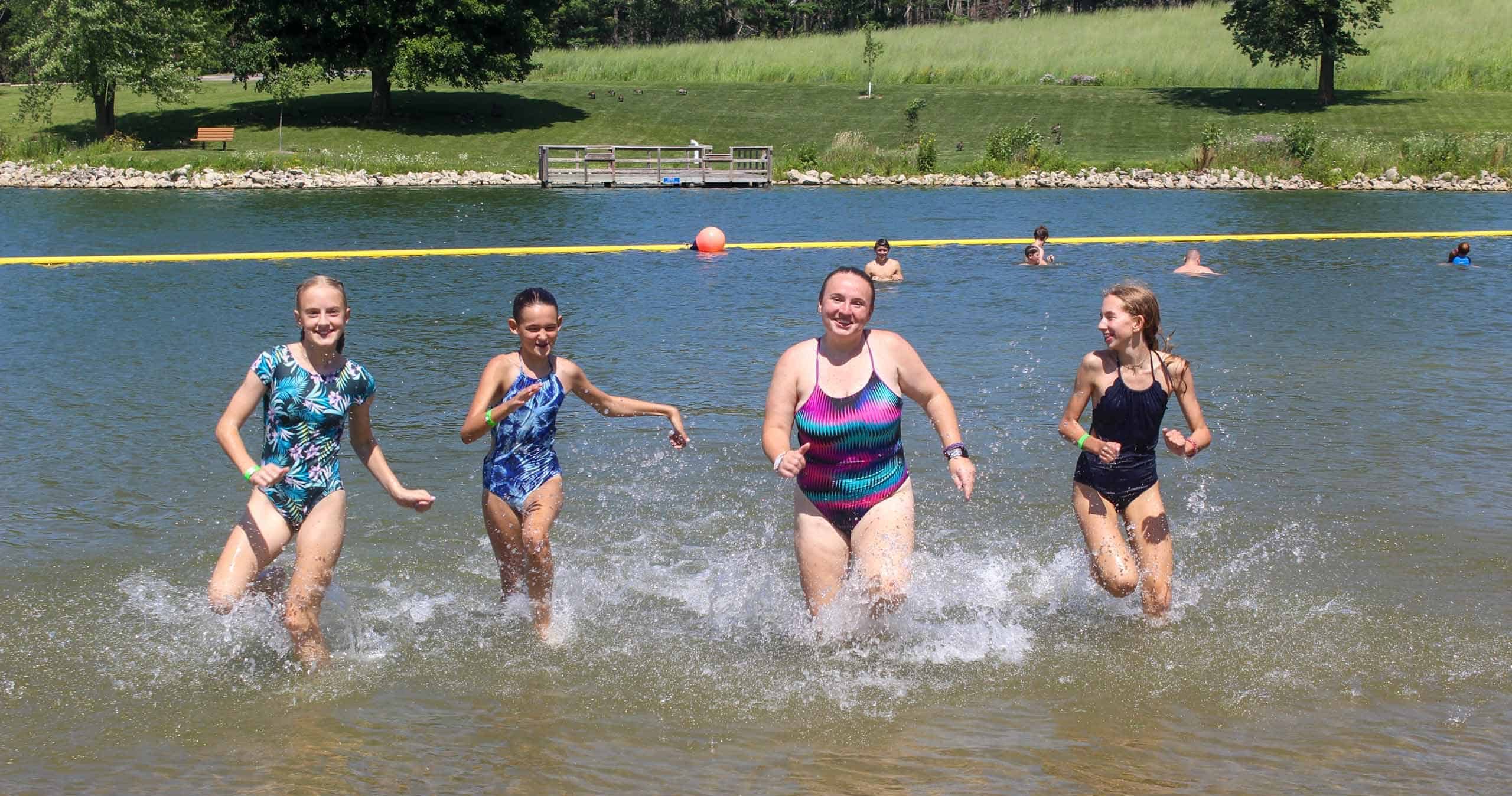 A group of kids running in the water at an Iowa summer camp.