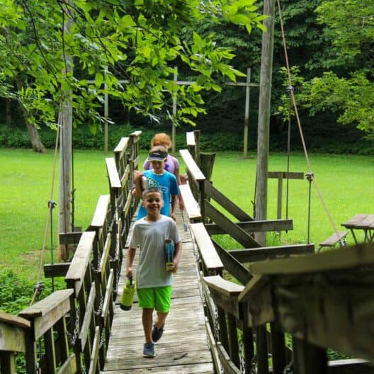 A group of kids walking on a wooden bridge during a summer camp in Iowa.
