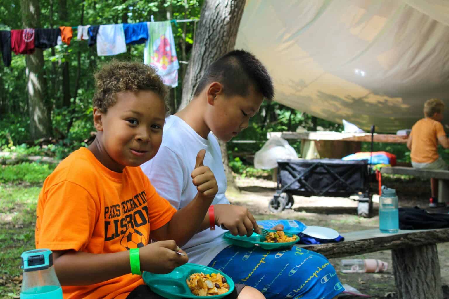 Two young boys at an Iowa summer camp eating plates of food.