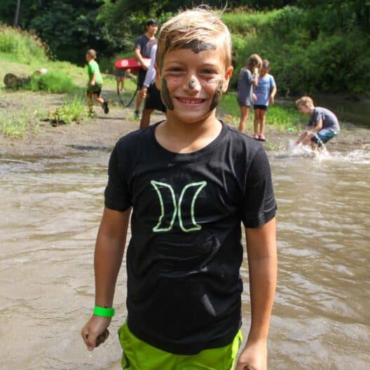 A kid in a green shirt standing in a river during summer camp in Iowa.