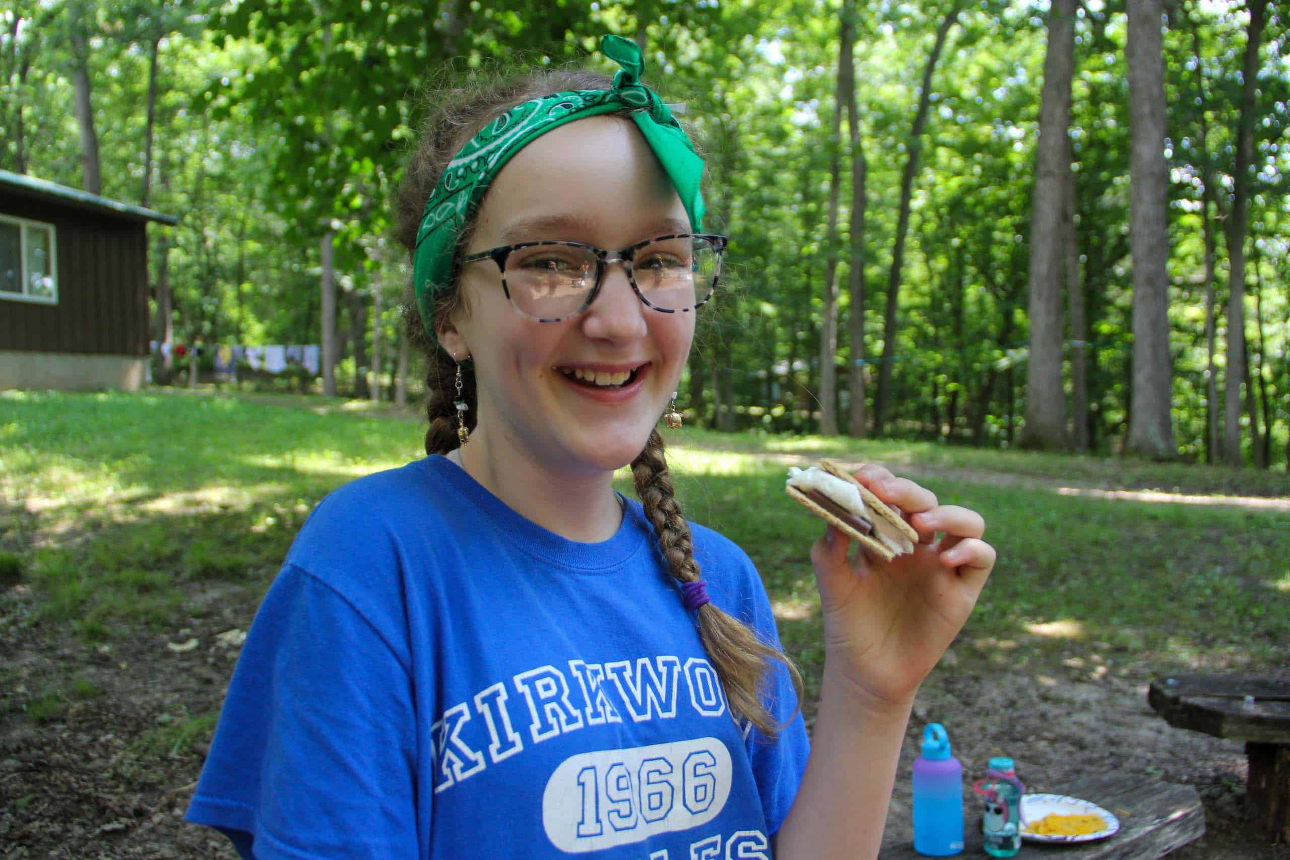 A girl with glasses eating a smore at summer camp in Iowa.