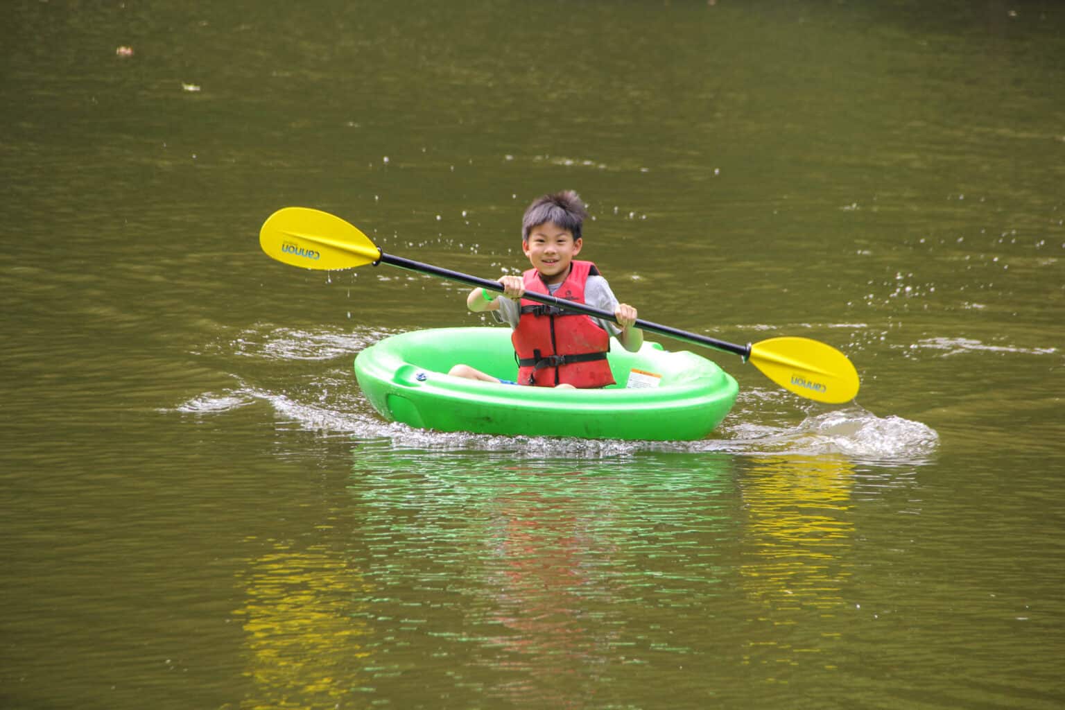 A young boy in Iowa is paddling a raft at summer camp.