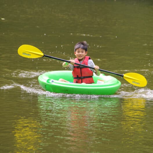 A young boy in Iowa is paddling a raft at summer camp.