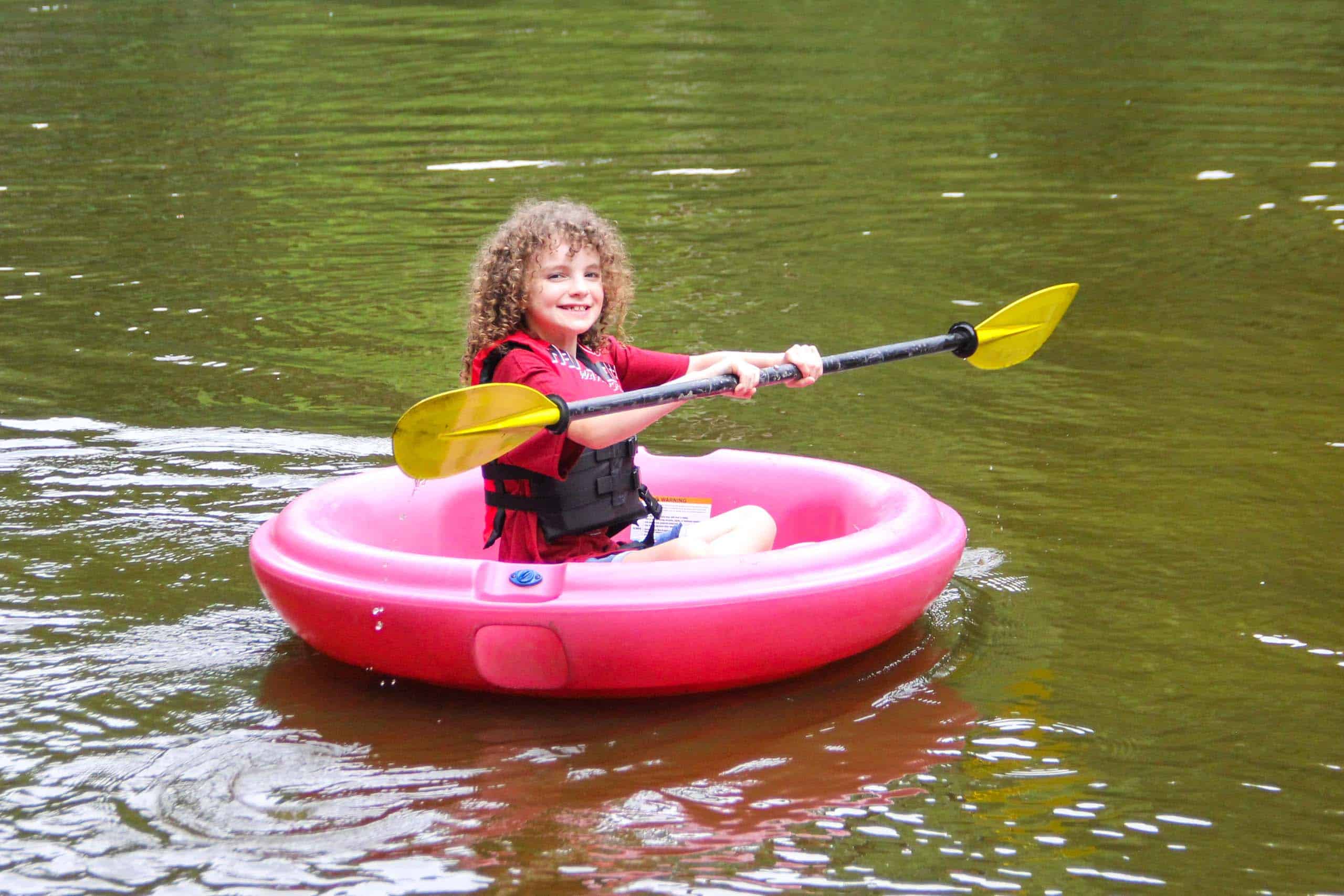 A kid at summer camp in Iowa floats on a pink raft in a body of water.