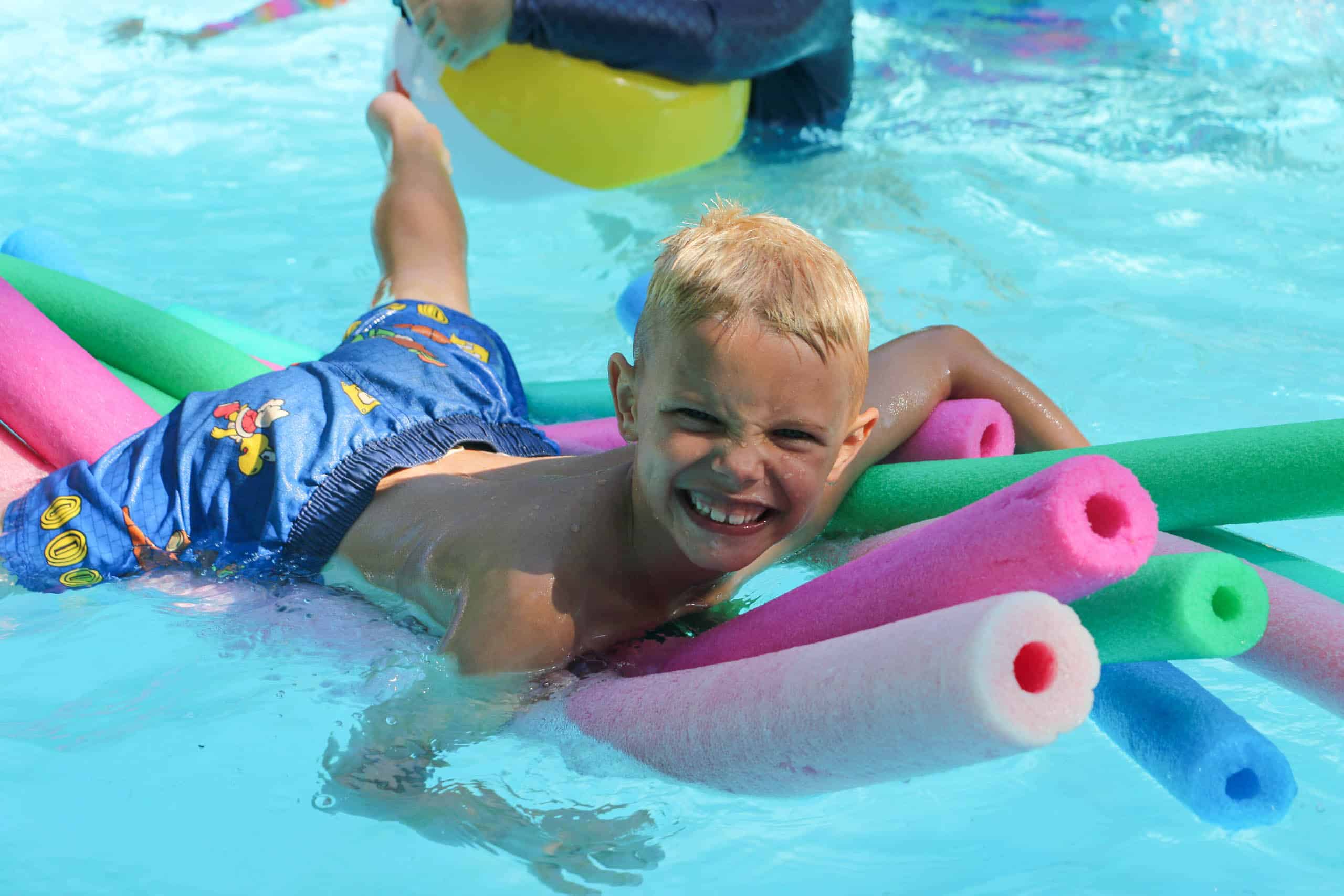 A young boy lays on colorful floats in a pool at summer camp in Iowa.