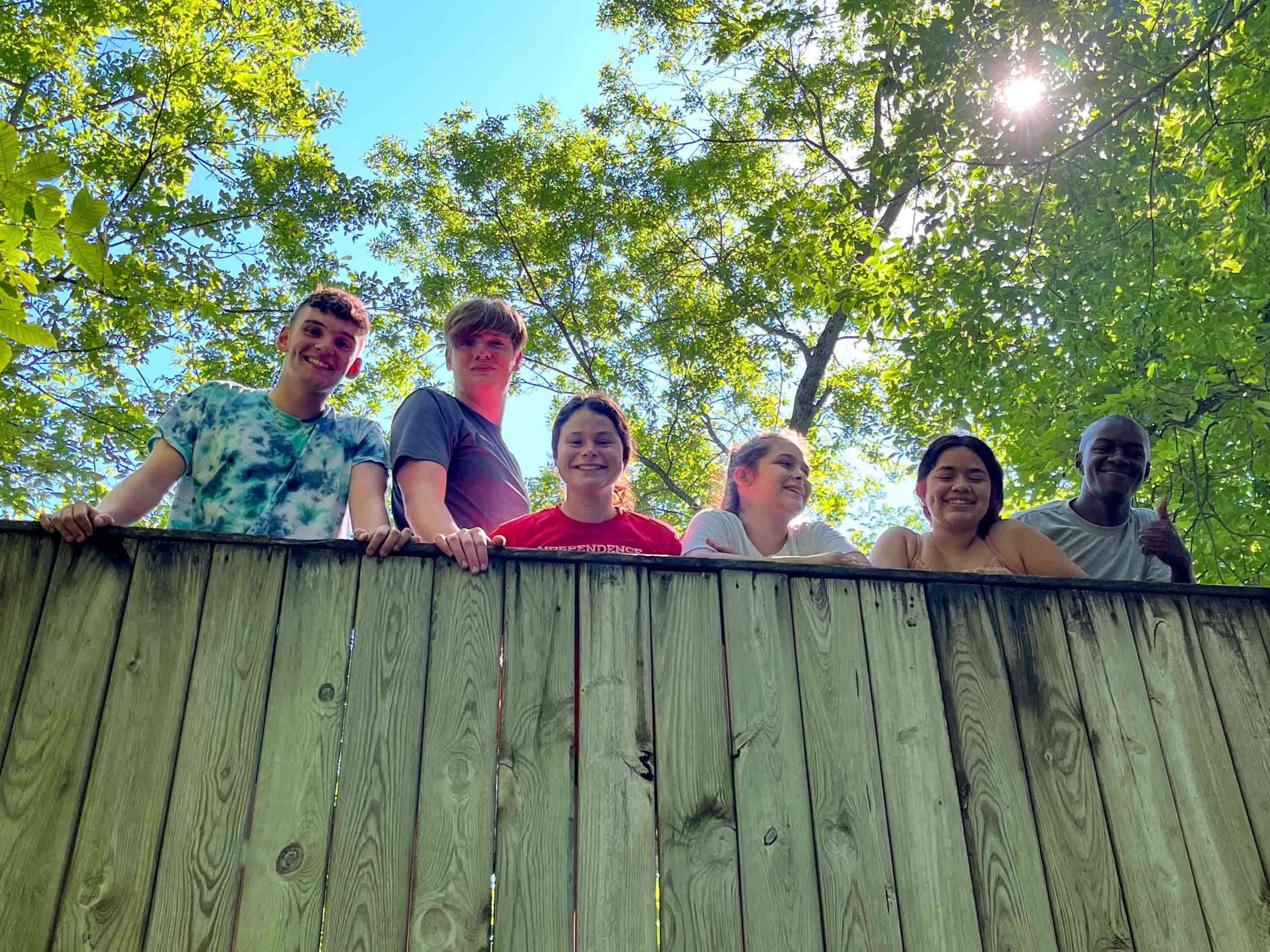 A group of kids standing on a wooden fence at an Iowa summer camp.