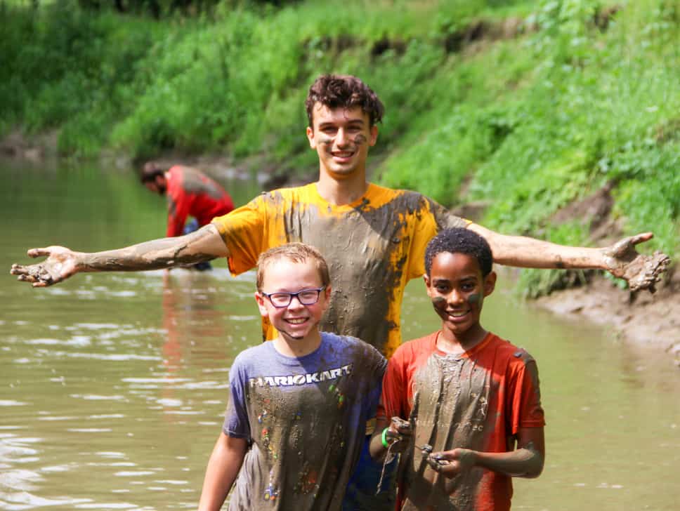 A group of kids at an Iowa summer camp standing in a muddy river.