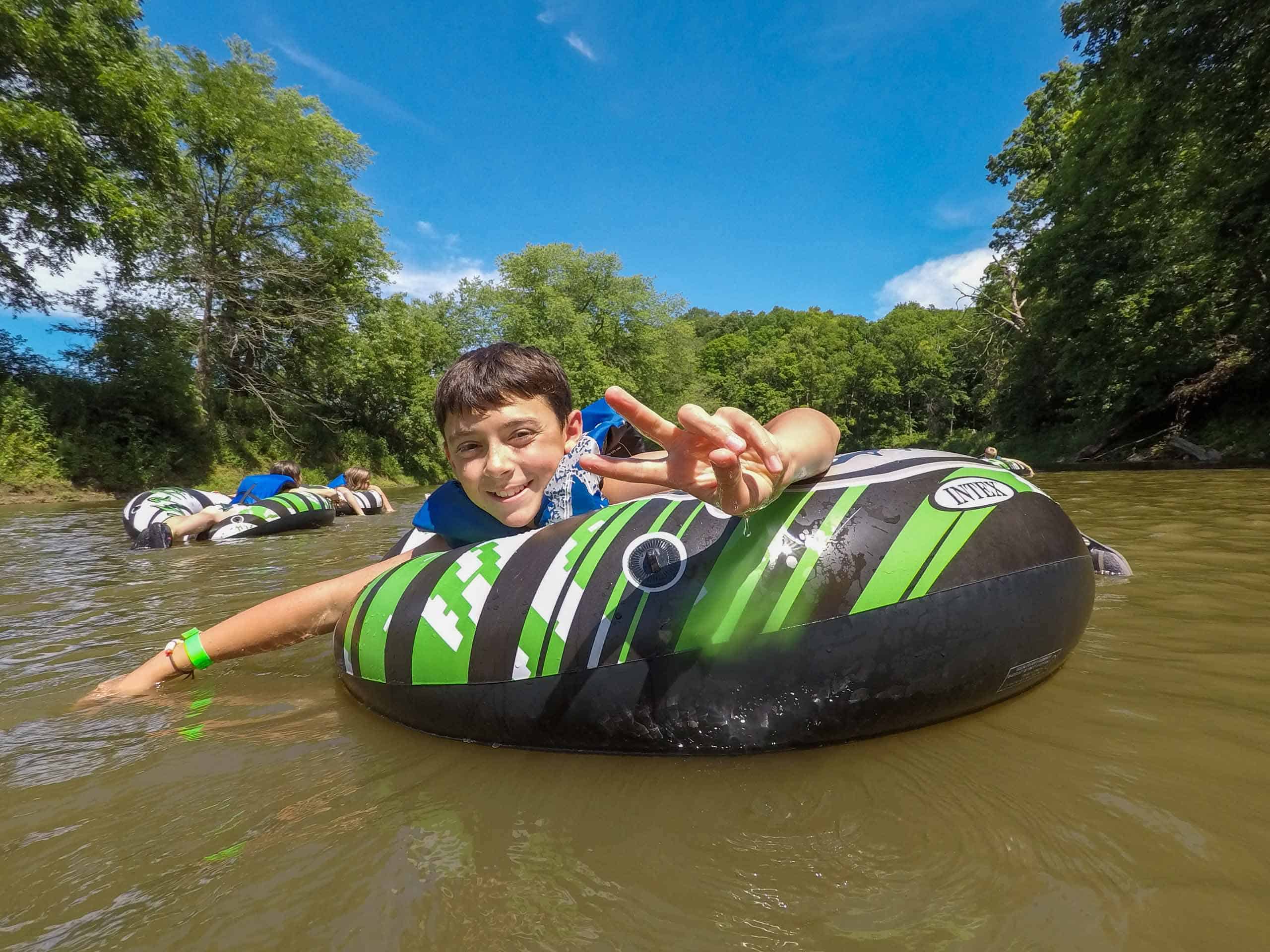 A boy is floating down a river on an inflatable tube at summer camp in Iowa.