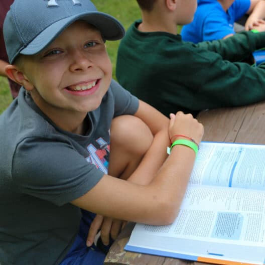 A boy studying a Bible during summer camp at a picnic table in Iowa.