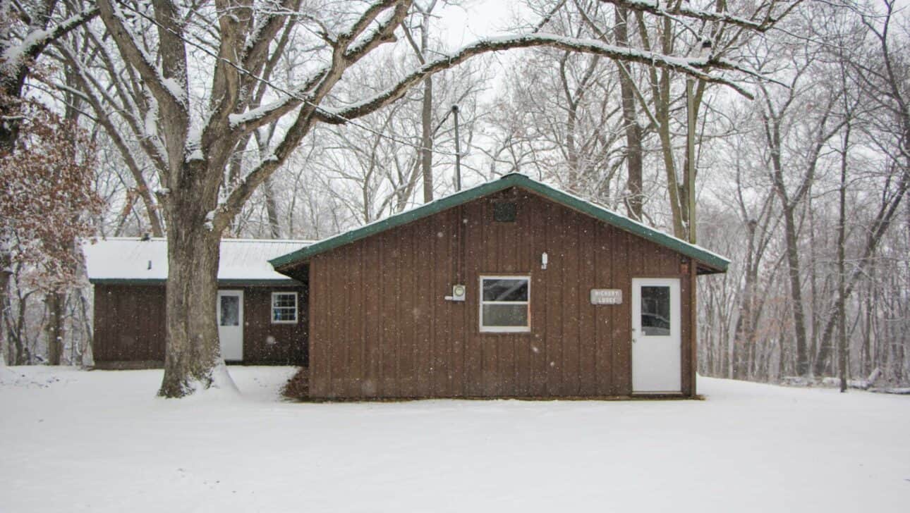 A summer camp cabin in the woods of Iowa with snow on the ground.