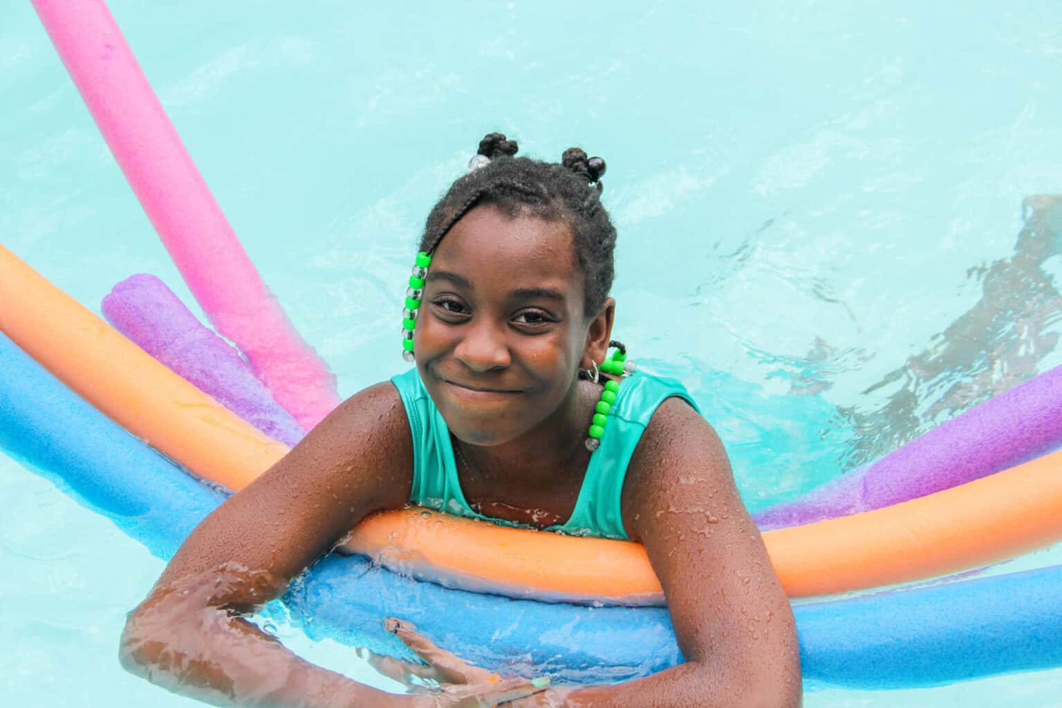 A young girl at a summer camp in Iowa enjoying a pool with colorful floats.