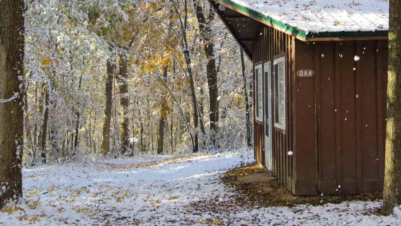 A summer camp cabin in the woods of Iowa covered in snow.