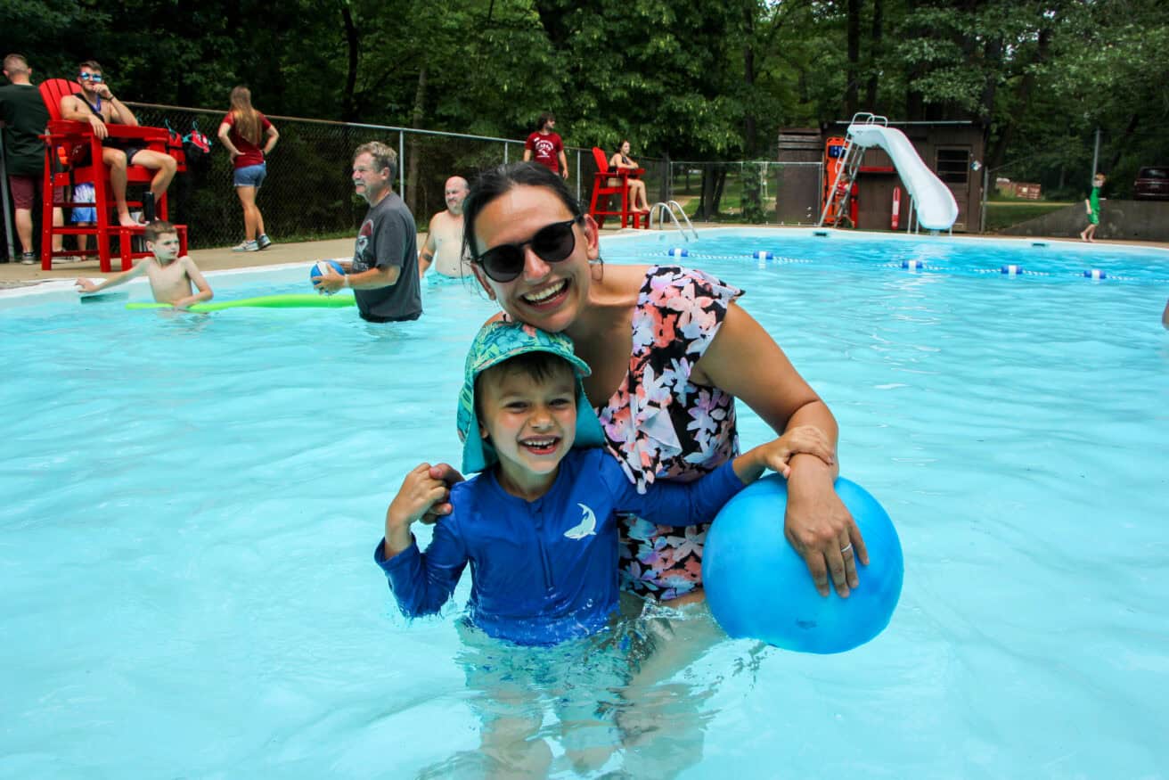 A parent and young camper pose together in the pool