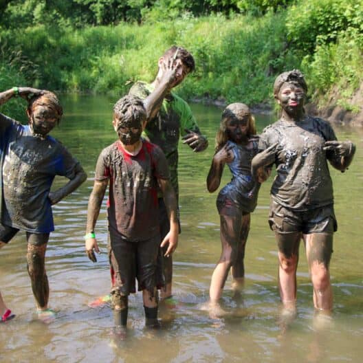 A group of kids at an Iowa summer camp standing in a river covered in mud.