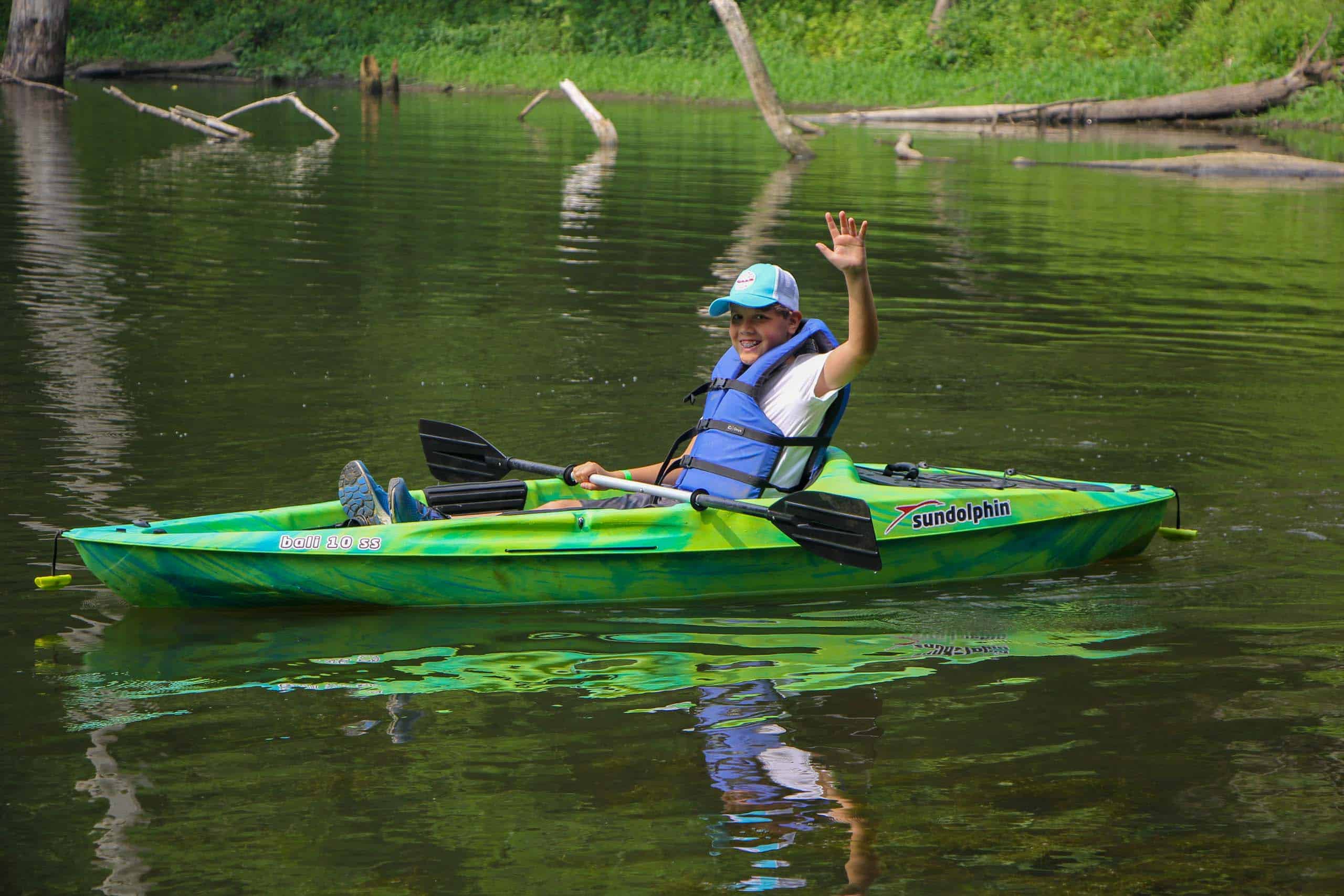 A young boy kayaking on a river in Iowa during summer camp.