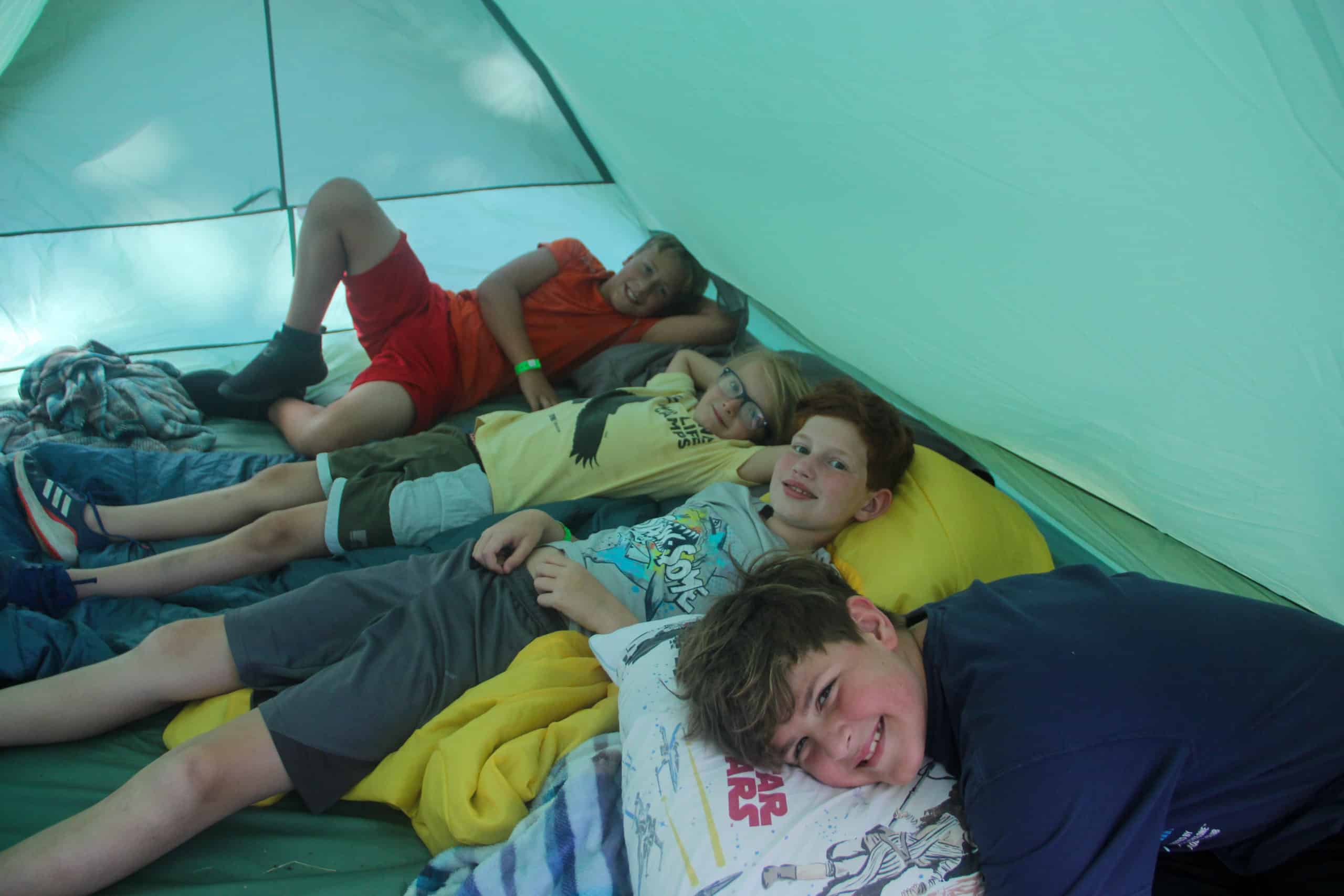 Four young boys laying on sleeping bags side by side in their tent.