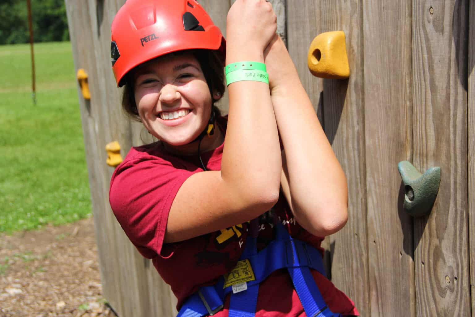 A girl wearing a helmet while climbing a rock wall at a summer camp in Iowa.