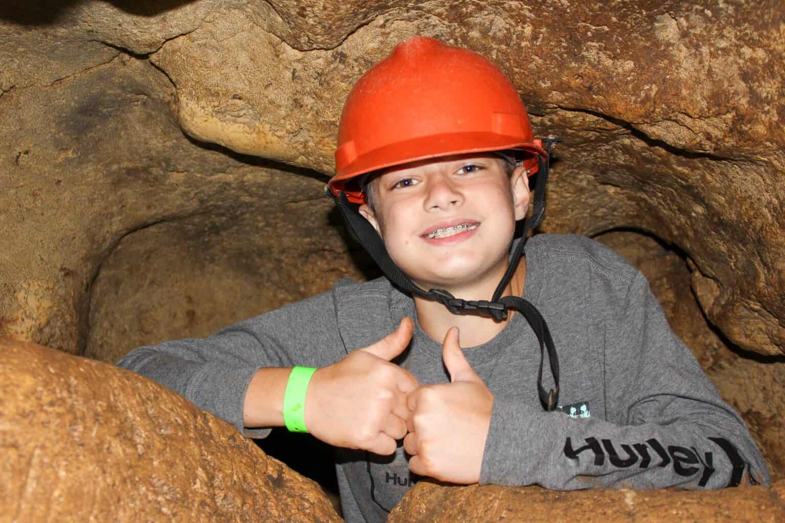 A young boy giving a thumbs up while in a cave during summer camp in Iowa.