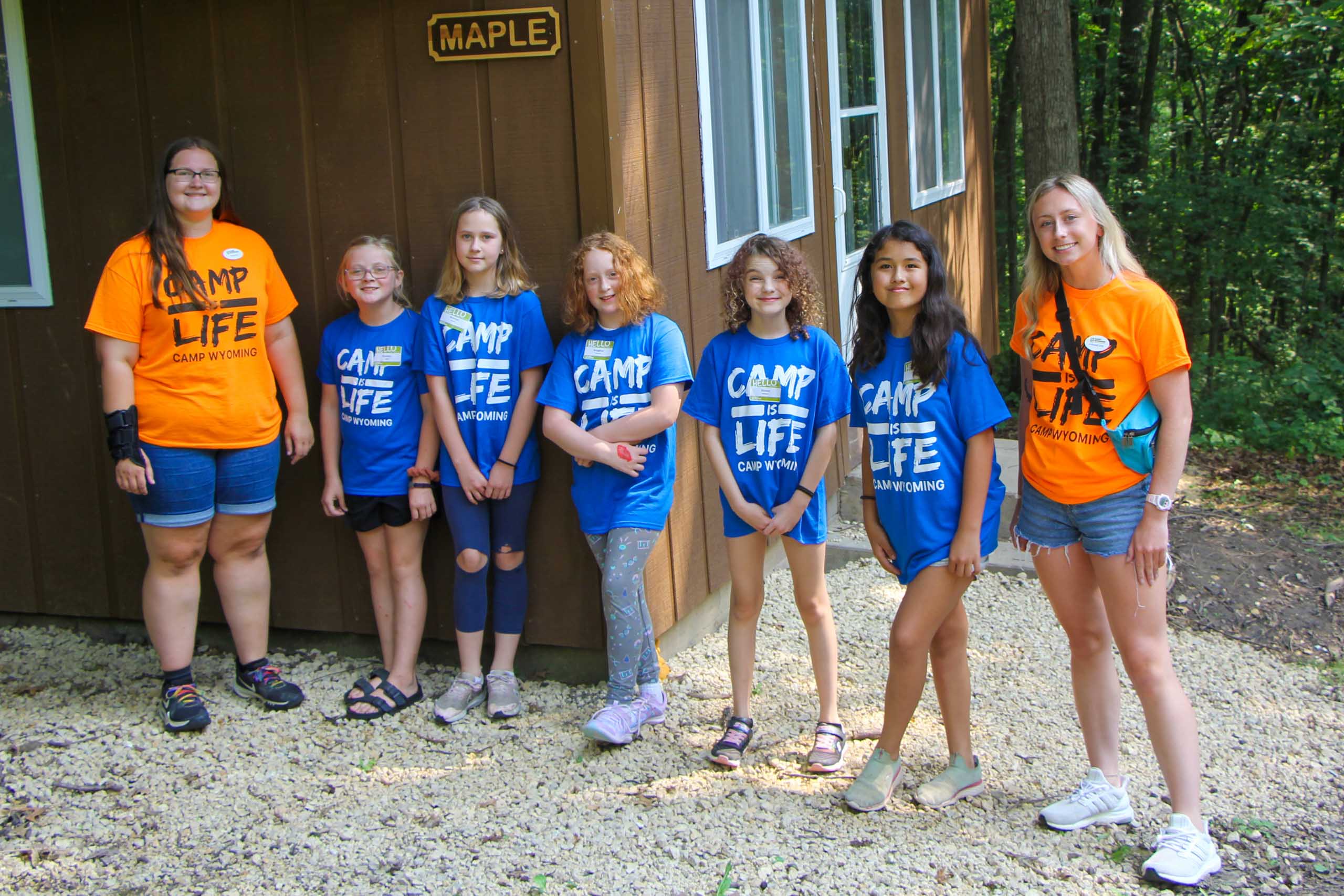 A group of kids posing in front of a cabin with their counselors during summer camp in Iowa.