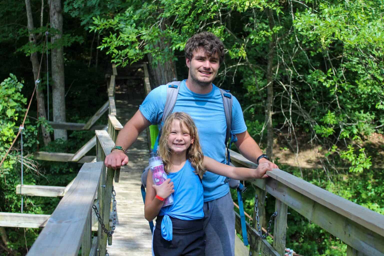 A girl standing on a wooden bridge with her summer camp counselor in the woods of Iowa.