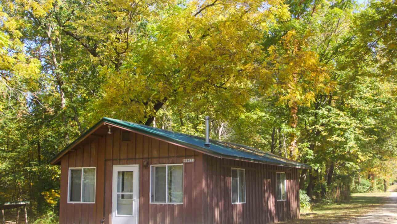 A small summer camp cabin surrounded by trees in a wooded area of Iowa.
