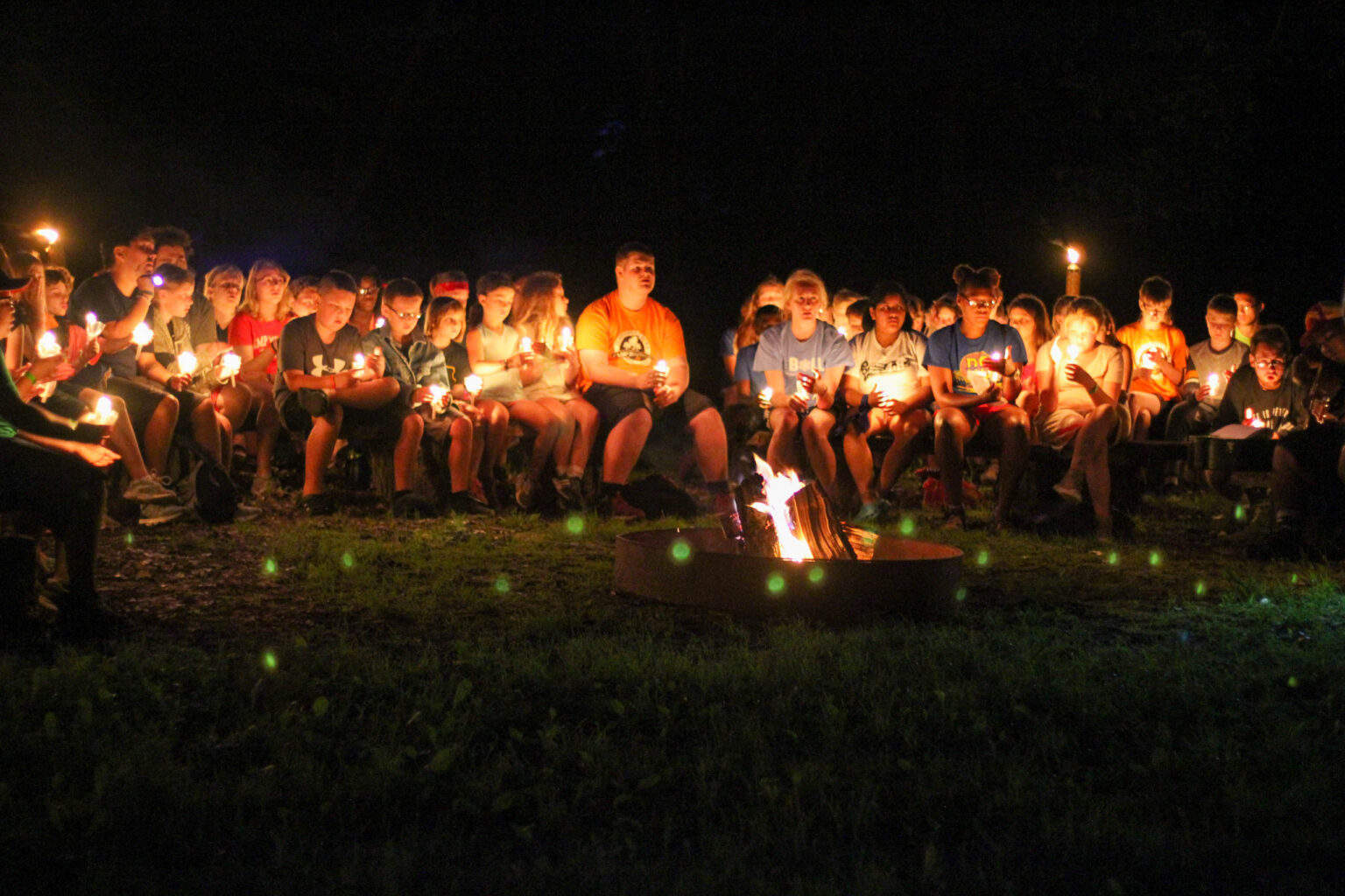 A group of kids sitting around a campfire at a summer camp in Iowa.