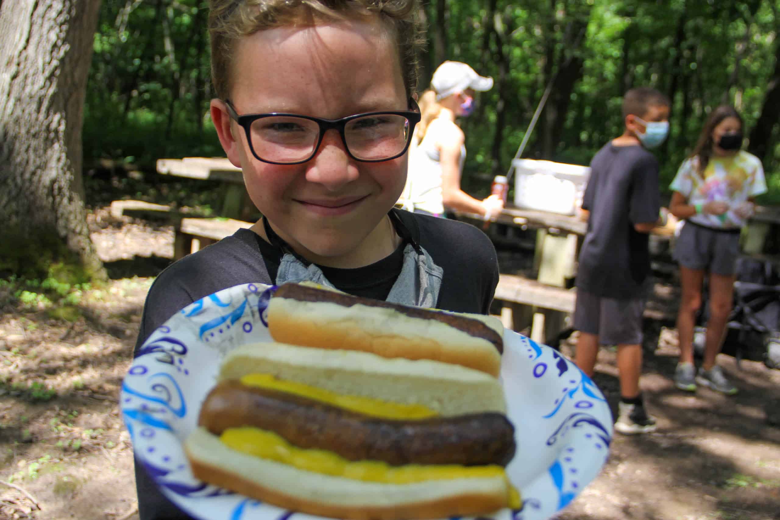 A boy at summer camp in Iowa holding a plate of hot dogs.