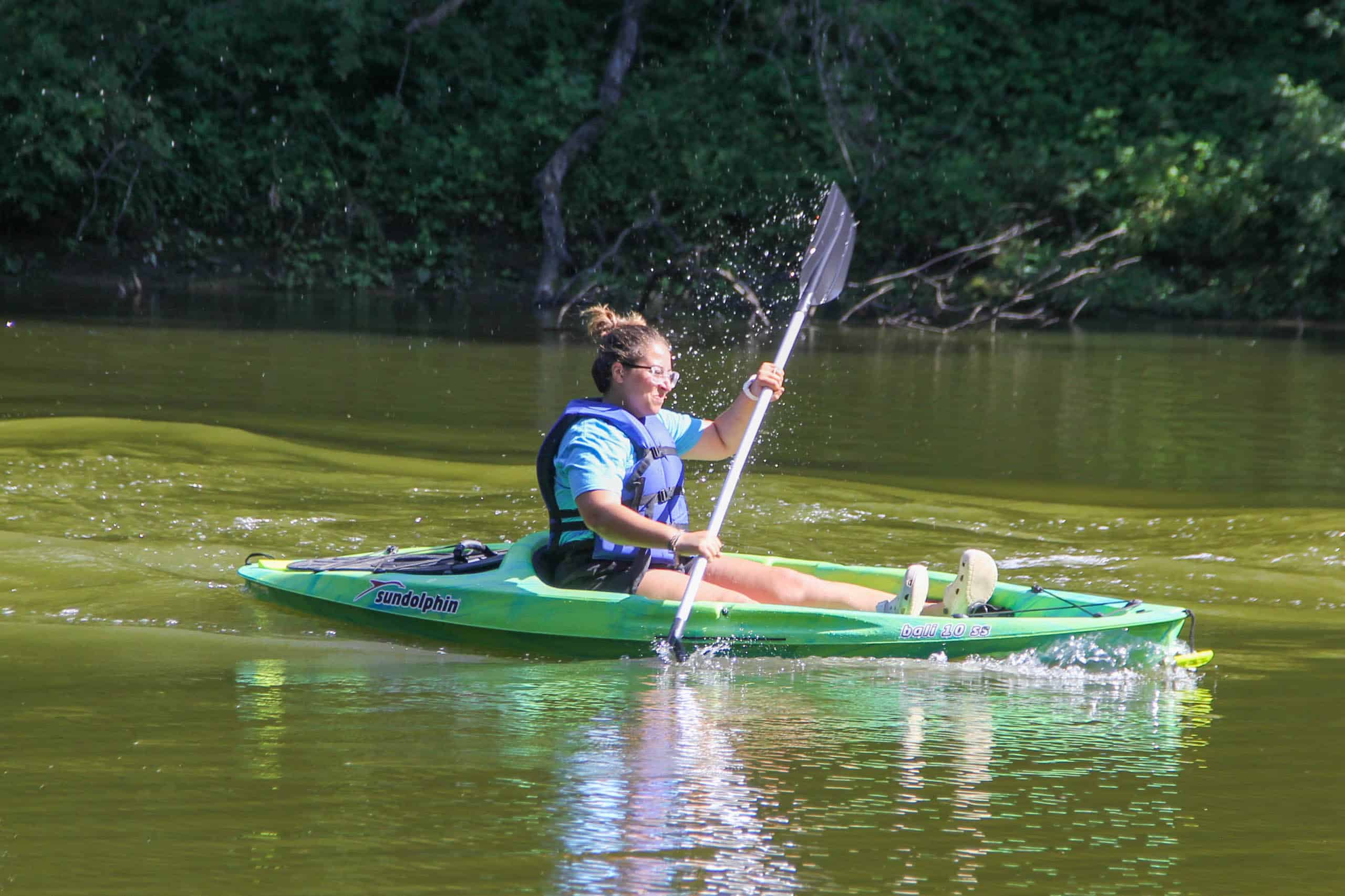 A girl is paddling a green kayak in Iowa during summer camp.