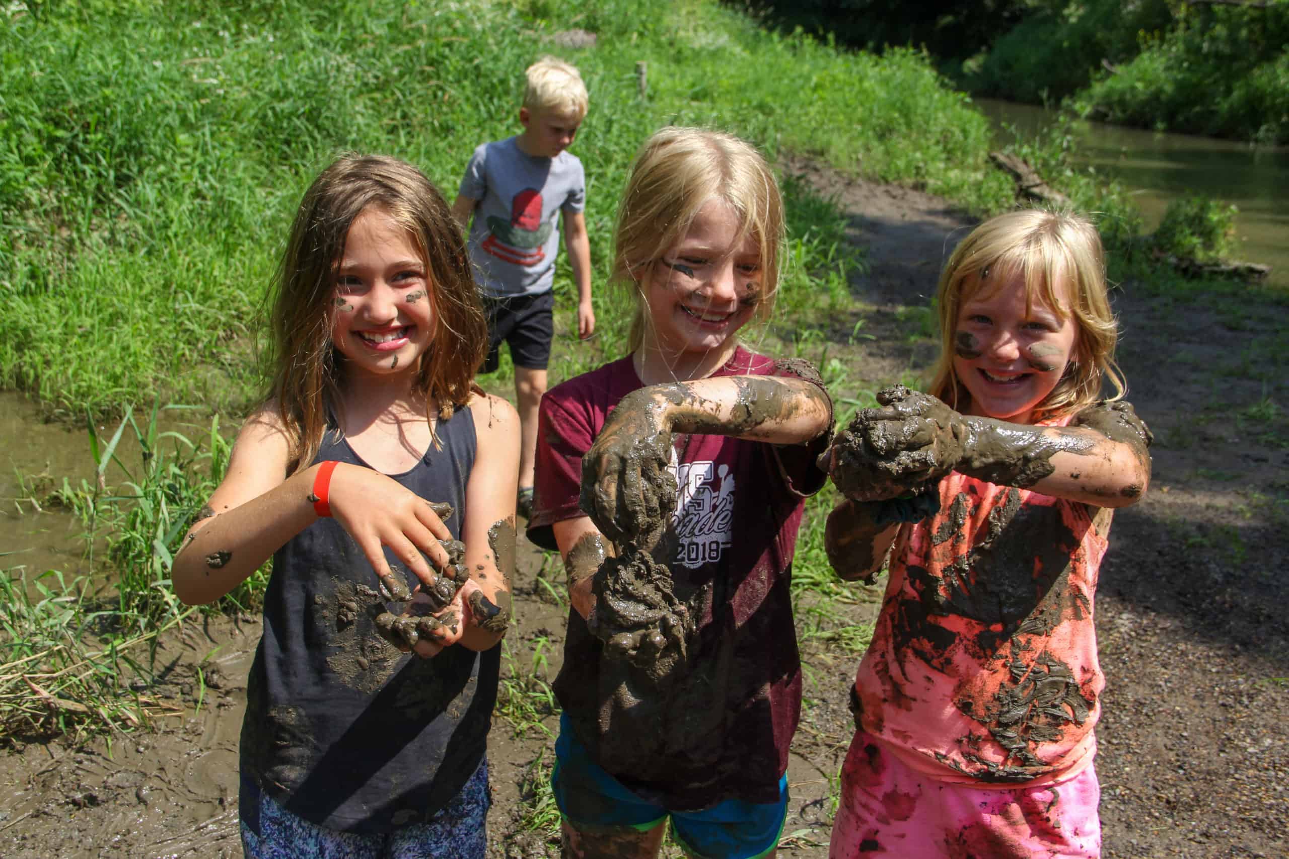 Three young girls playing in the mud together at the creek.