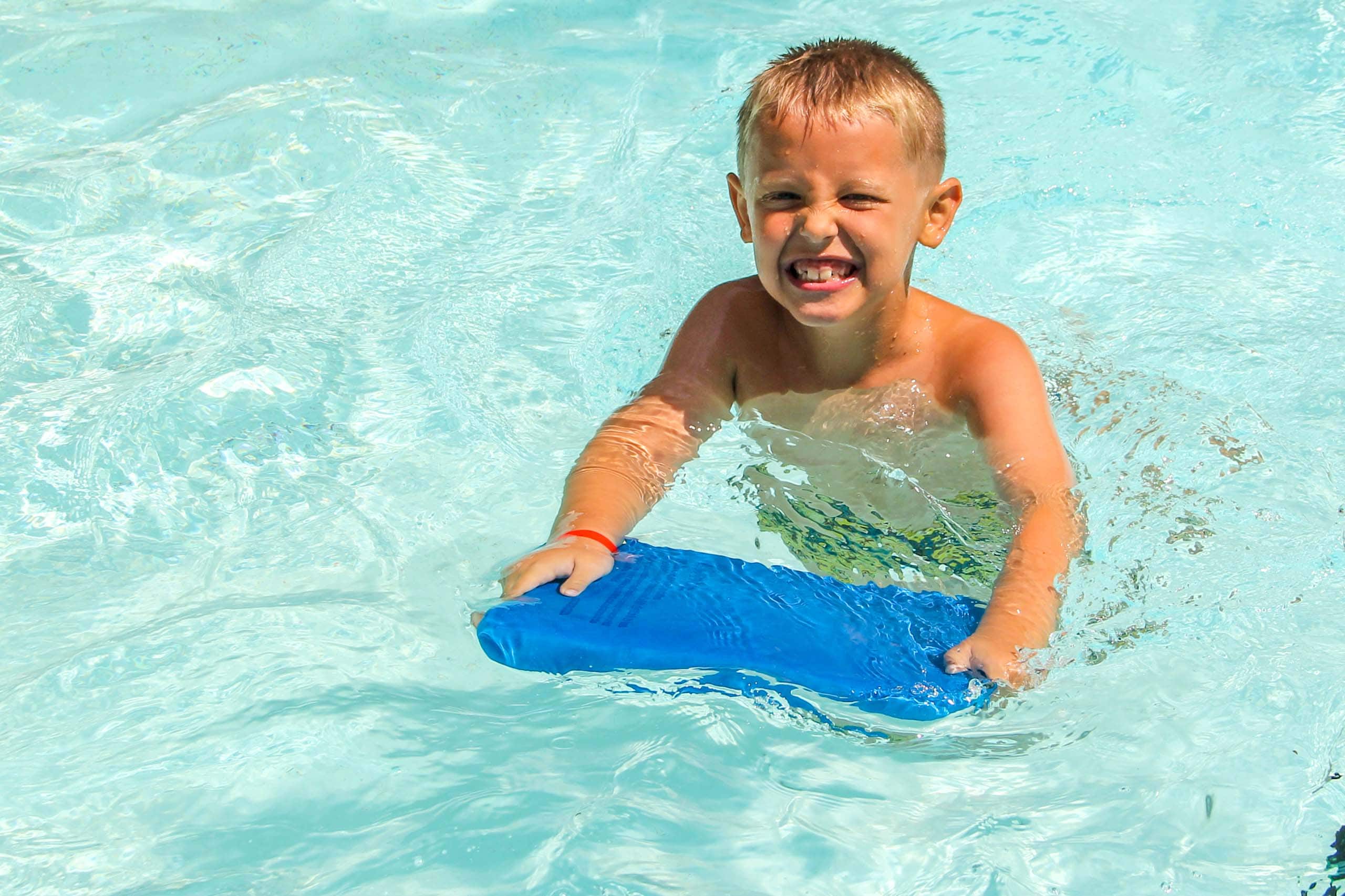 A young boy at an Iowa summer camp in a pool holding a blue pool float.