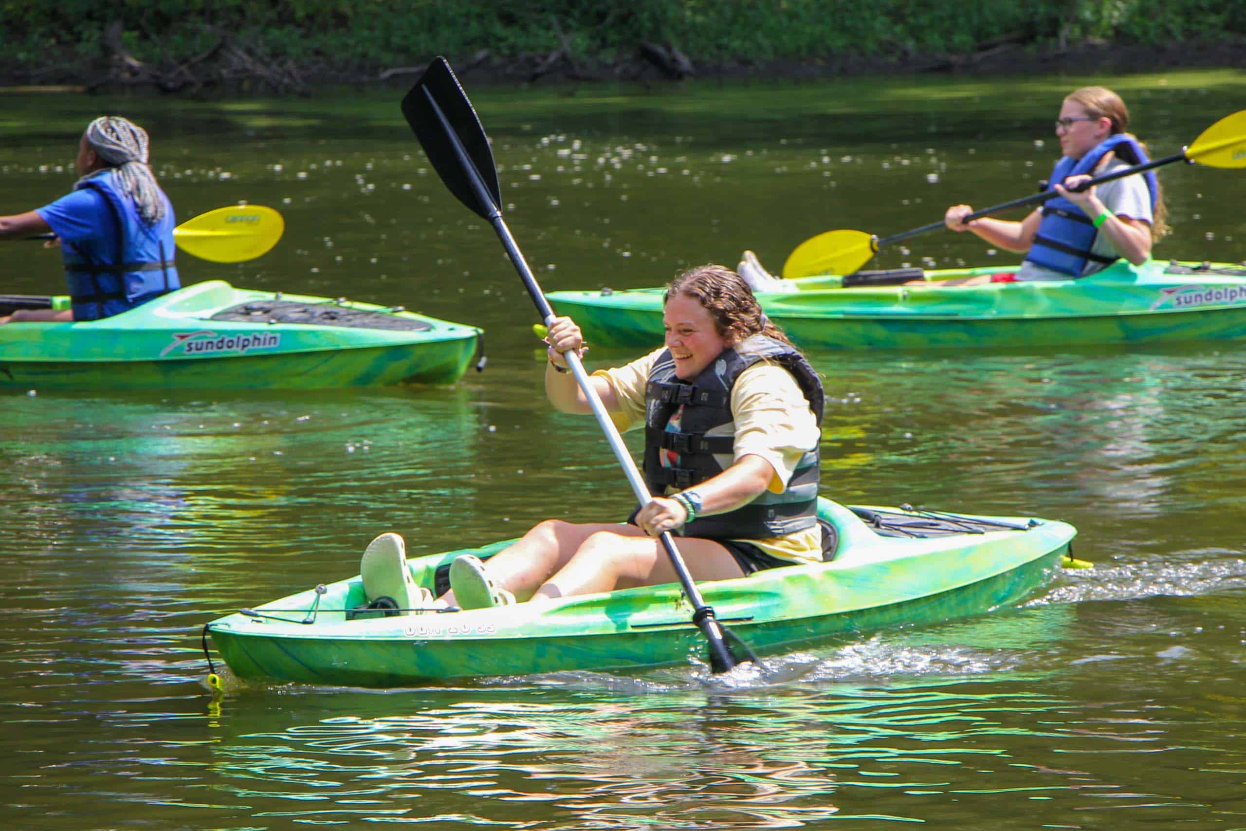 A group of kids paddling kayaks at a summer camp in Iowa.