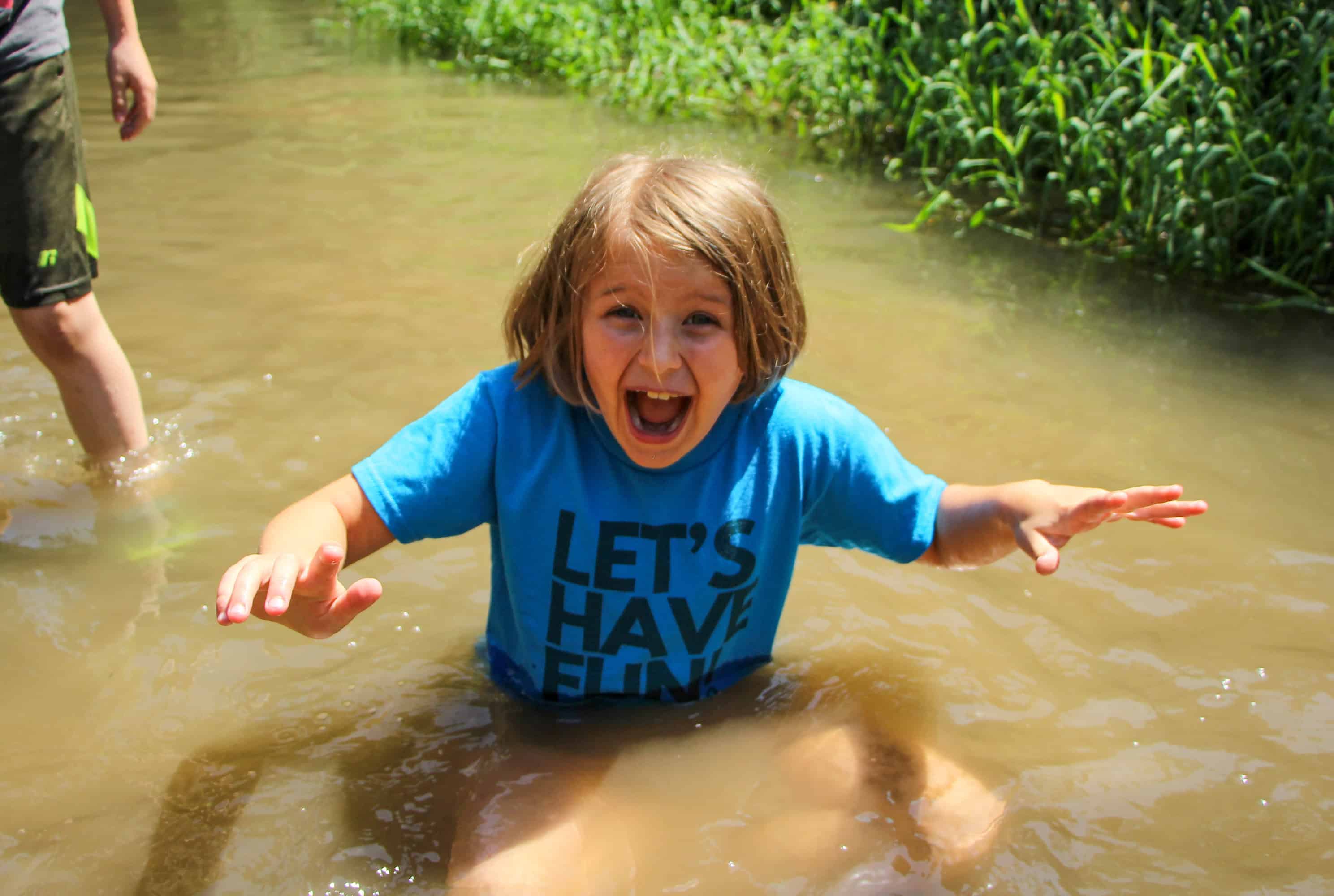 A young girl laughs with delight while sitting in the creek