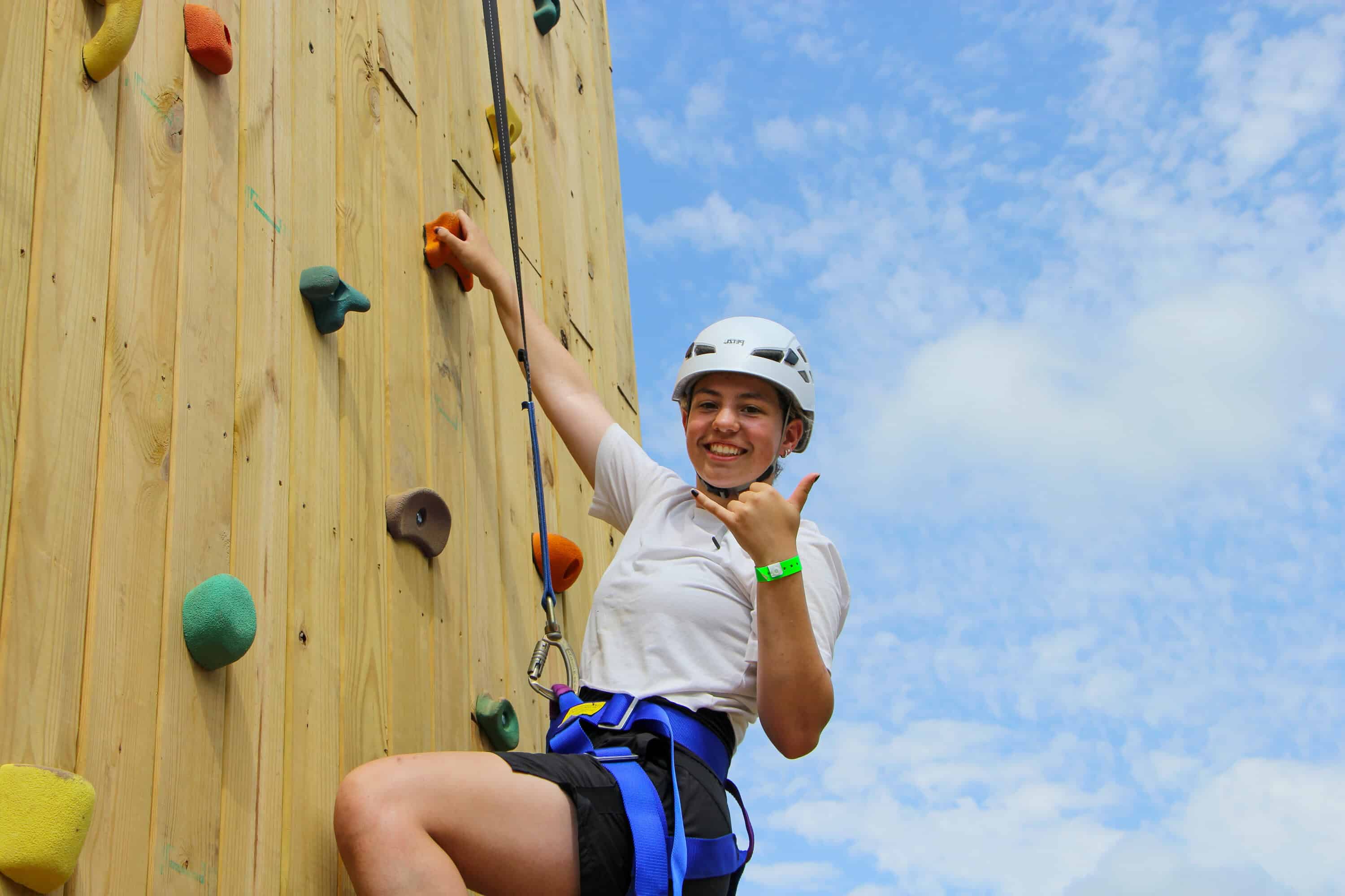 A teen girl flashes a surf's up sign from the climbing tower